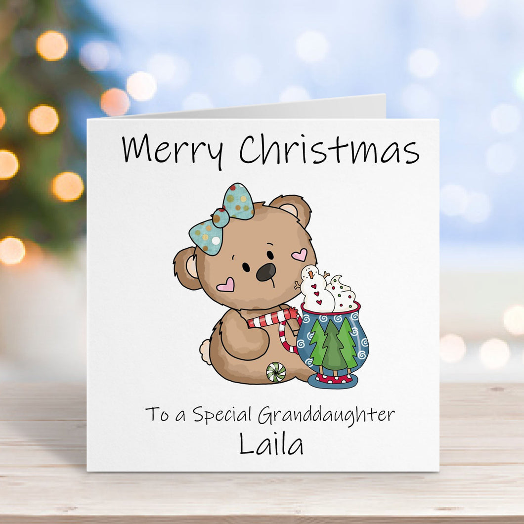 Christmas card with a teddy bear holding a gift, personalized for a special granddaughter, on a blurred festive background.
