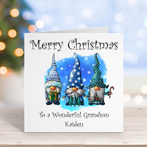 Christmas card with three gnomes and personalized text on a wooden surface with blurred lights in the background.