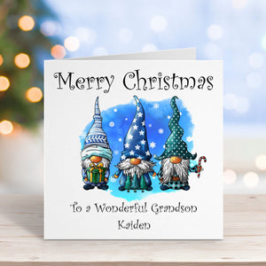 Christmas card with three gnomes and personalized text on a wooden surface with blurred lights in the background.