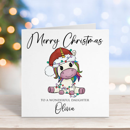 Christmas card with a unicorn design and personalized text on a wooden surface with blurred lights in the background.