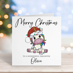 Christmas card with a unicorn design and personalized text on a wooden surface with blurred lights in the background.